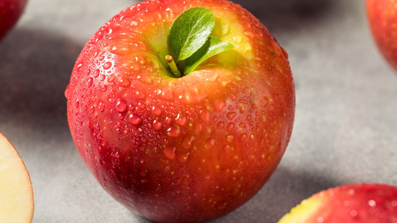 A bright and vibrant red Cosmic Crisp® fruit sitting beside other fruits, appearing wet with water drops on its skin