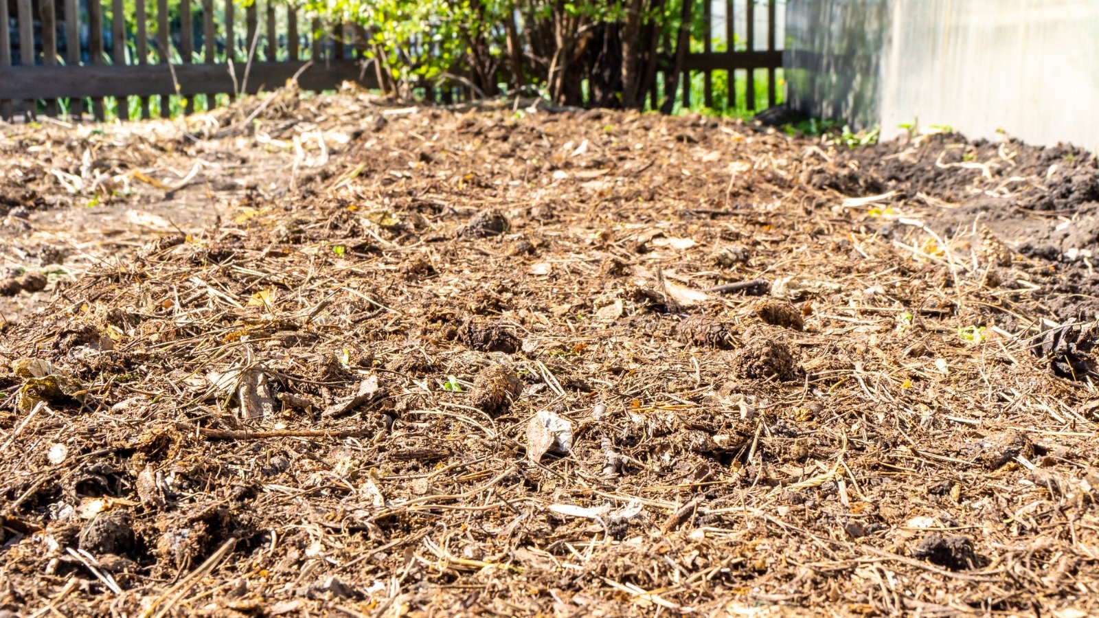 Close-up of a garden bed covered with a layer of mulch made of dry grass, leaves, and branches to protect the soil from frost.
